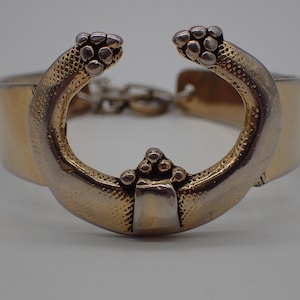 Peut inclure: Un bracelet en or et argent avec un design unique composé de deux bras incurvés à surface texturée et d'une pièce centrale avec un groupe de petits cercles.