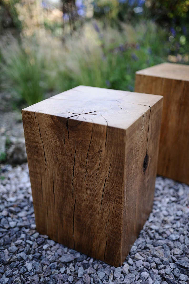 May include: Two wooden stools made from rough-hewn logs. The stools are square and have a natural wood finish. They are sitting on a bed of small gray stones.
