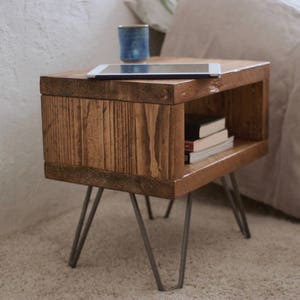 May include: A wooden end table with a shelf and hairpin legs. The table is made of reclaimed wood and has a natural finish. A tablet and books are on the table.