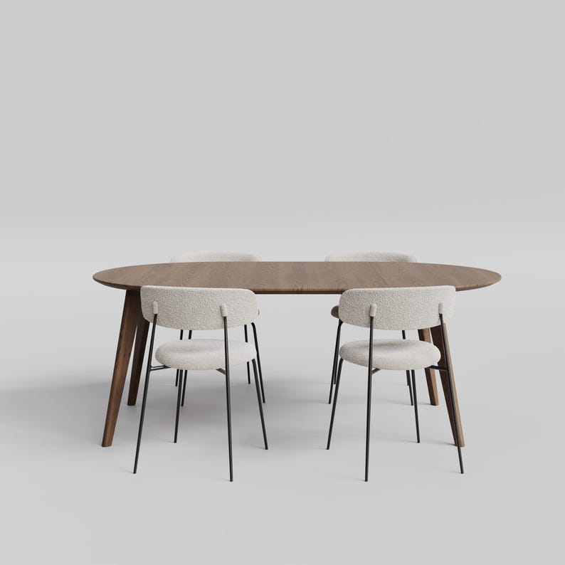 May include: An oval wooden dining table with a dark brown finish and four angled legs, accompanied by four chairs featuring off-white textured fabric seats and backrests supported by thin black metal frames arranged around the table.