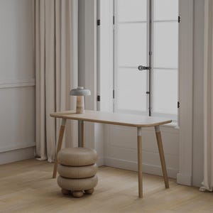 Può includere: Una scrivania in legno chiaro con bordi arrotondati e quattro gambe affusolate, accompagnata da uno sgabello in legno abbinato a tre livelli arrotondati con piccoli piedini sferici. Una piccola lampada da tavolo con base in pietra e paralume grigio.
