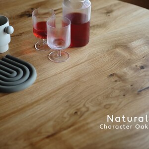 Puede incluir: Una superficie de mesa de roble natural con una taza beige claro con un detalle esf&eacute;rico lateral, dos vasos de vidrio estriado, una jarra de vidrio estriado con l&iacute;quido rojo y un salvamanteles de silicona gris oscuro con el texto Natural Character Oak.