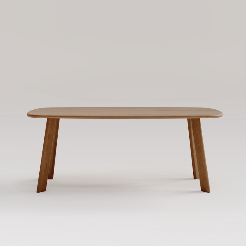 May include: A light brown wooden table with a rectangular top and four angled legs. The table has rounded corners and a smooth finish. The legs are slightly tapered, giving the table a modern look. The table is approximately 60 inches long.
