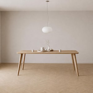 Könnte beinhalten: Ein heller Holzesstisch mit vier konisch zulaufenden Beinen, darauf eine weiße Keramik-Teekanne, eine kleine Vase mit einem getrockneten Zweig und zwei kleine Tassen auf einem Tablett, beleuchtet von einer weißen, ovalen Hängeleuchte.