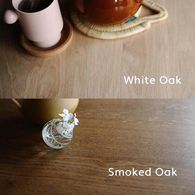May include: A split image showcasing two types of wood: White Oak and Smoked Oak. The top half features a light-colored wood with a pink mug and a brown mug on a woven coaster. The bottom half displays a darker wood with a small glass vase.