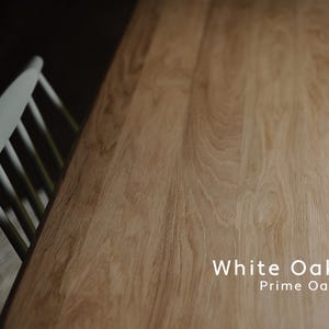 May include: A close-up of a light-colored wooden table with visible wood grain. The text "White Oak Prime Oak" is displayed on the table. A white chair is partially visible in the upper left corner.