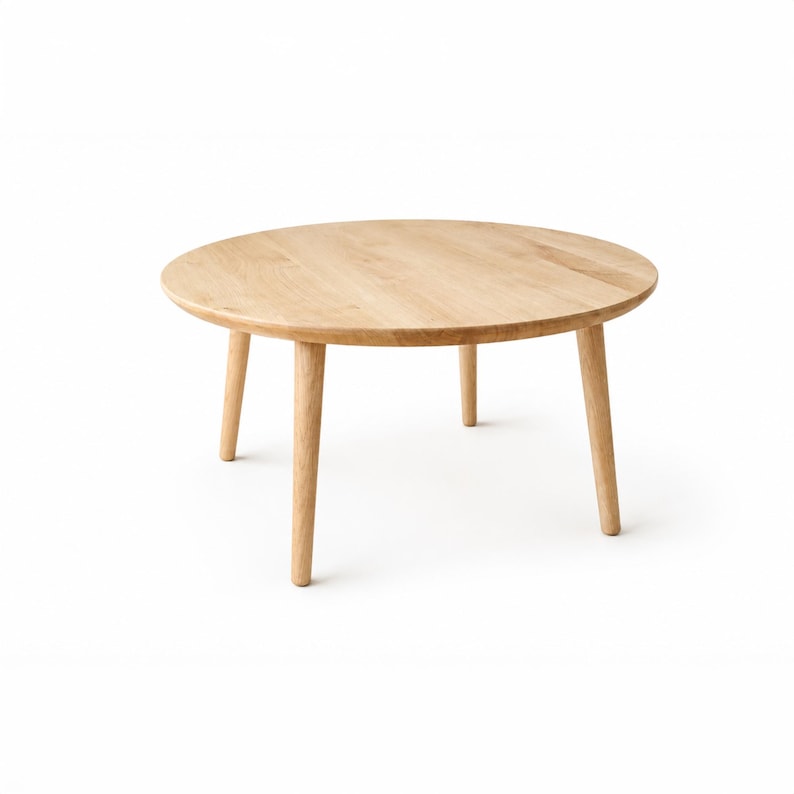 Puede incluir: Una mesa de centro redonda de madera clara con cuatro patas c&oacute;nicas. La superficie de la mesa tiene un acabado de veta de madera natural. La mesa se presenta sobre un fondo blanco, resaltando su dise&ntilde;o sencillo y moderno.