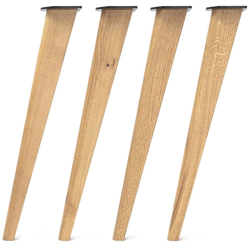 May include: A set of four tapered furniture legs crafted from light-toned wood with a visible natural grain pattern. Each leg features a flat, black metal mounting plate at the top, angled to provide a slanted orientation for furniture support.
