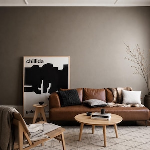 Puede incluir: Un sal&oacute;n con un sof&aacute; de cuero marr&oacute;n, cojines y una manta de piel. Una mesa de centro redonda de madera con libros y un cuenco. Una obra de arte enmarcada con la palabra "chillida" cuelga de la pared. Paleta de colores neutros.