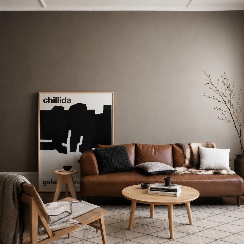 Puede incluir: Un sal&oacute;n con un sof&aacute; de cuero marr&oacute;n, cojines y una manta de piel. Una mesa de centro redonda de madera con libros y un cuenco. Una obra de arte enmarcada con la palabra "chillida" cuelga de la pared. Paleta de colores neutros.