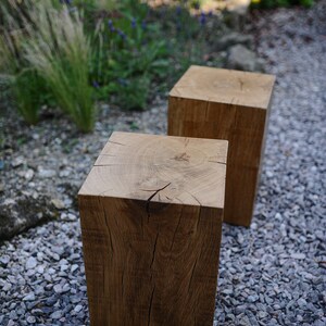 May include: Two wooden stools made from rough-hewn oak logs, sitting on a bed of gray gravel. The stools are natural wood color with visible grain and knots.