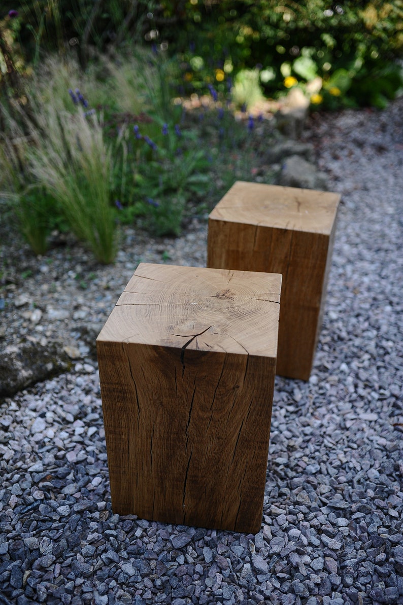 May include: Two wooden stools made from rough-hewn oak logs, sitting on a bed of gray gravel. The stools are natural wood color with visible grain and knots.