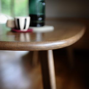 May include: A close-up of a wooden table with a rounded edge. A white cup with black stripes sits on a red coaster. A green bottle is visible in the background. The table has a natural wood grain.