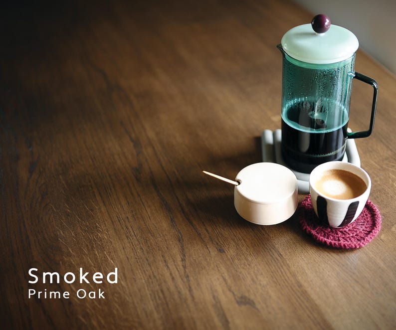 Puede incluir: Una cafetera de &eacute;mbolo con tapa verde claro y asa negra sobre un posavasos gris. Un azucarero blanco peque&ntilde;o con cuchara de madera y una taza de caf&eacute; con dise&ntilde;o blanco y negro sobre mesa de madera. Un posavasos rojo bajo la taza. El texto "Smoked Prime Oak" est&aacute; en la parte inferior.