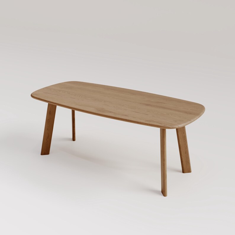 May include: A light brown wooden coffee table with a rectangular top and rounded corners. The table has four angled legs. The wood grain is visible on the surface. The table is approximately 60 inches long.