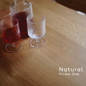 Puede incluir: Una botella de vidrio transparente y tres vasos sobre una mesa de roble natural. Dos vasos contienen un l&iacute;quido rojo. Los vasos y la botella tienen detalles acanalados verticales. El texto "Natural Prime Oak" es visible.