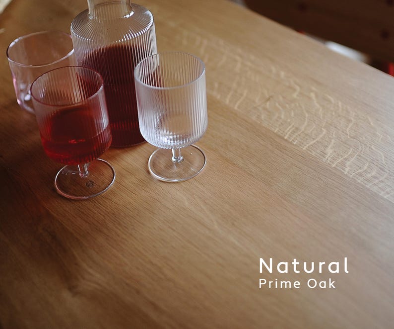 Puede incluir: Una botella de vidrio transparente y tres vasos sobre una mesa de roble natural. Dos vasos contienen un l&iacute;quido rojo. Los vasos y la botella tienen detalles acanalados verticales. El texto "Natural Prime Oak" es visible.