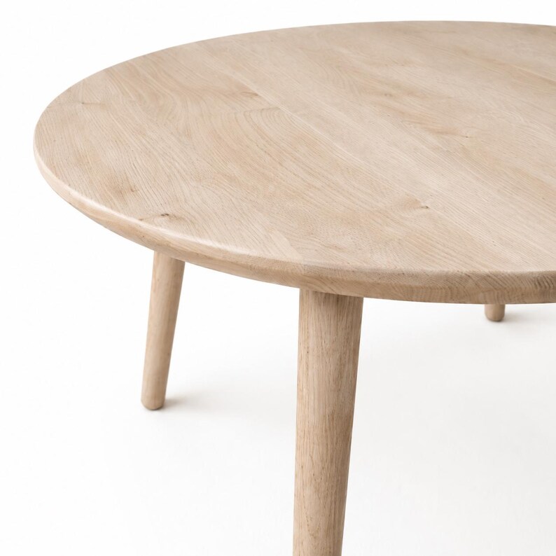 Puede incluir: Una mesa de centro redonda de madera clara con cuatro patas c&oacute;nicas. La mesa tiene un acabado liso y natural con vetas de madera. Las patas est&aacute;n espaciadas uniformemente y proporcionan una base estable.