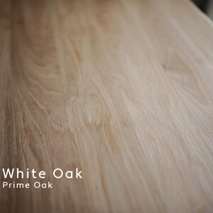 May include: Close-up of a light-colored, textured wood surface. The grain of the wood is visible, with a natural pattern of lines and swirls. The text "White Oak Prime Oak" is displayed in white.