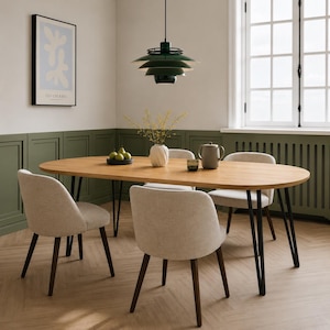 Puede incluir: Un comedor moderno con una mesa ovalada de madera clara y patas de metal negro, rodeada de cuatro sillas beige tapizadas. Una lámpara colgante verde cuelga sobre la mesa. Un jarrón con flores y una tetera están sobre la mesa.