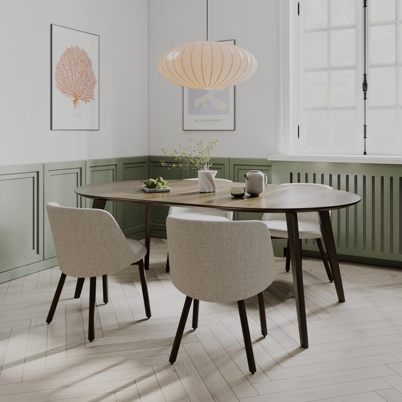 May include: A dining set featuring an oval wooden table with dark brown tapered legs and four upholstered chairs in a light beige fabric. The table is set with a small white vase containing greenery, a small bowl, and a grey ceramic pitcher.
