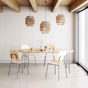 May include: An oval wooden dining table with four light-colored wooden chairs featuring thin metal legs. Three cylindrical woven rattan pendant lights hang above the table. On the table are a small ceramic vase, a teapot, and two small cups.