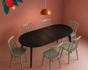 May include: An oval dark wood dining table surrounded by five light green spindle-back chairs. Above the table hangs a single orange dome pendant light. A decorative graphic of a red ornament with green leaves is in the top left corner.