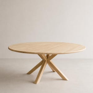 Könnte beinhalten: Runder Esstisch aus hellem Holz. Der Tisch hat eine runde Tischplatte und ein markantes Untergestell aus sich kreuzenden Holzbalken. Das Design ist schlicht und modern, mit einer natürlichen Holzmaserung. Durchmesser ca. 120 cm.