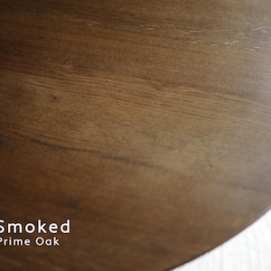 May include: A circular wooden surface featuring a dark brown, smooth grain pattern. The text "Smoked Prime Oak" is printed in white in the lower left corner, indicating the material and finish of the wood grain visible in this close-up view.