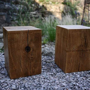 Puede incluir: Dos taburetes de madera rústica hechos de madera recuperada con un acabado marrón natural. Los taburetes están sentados en un lecho de pequeñas gravas grises.