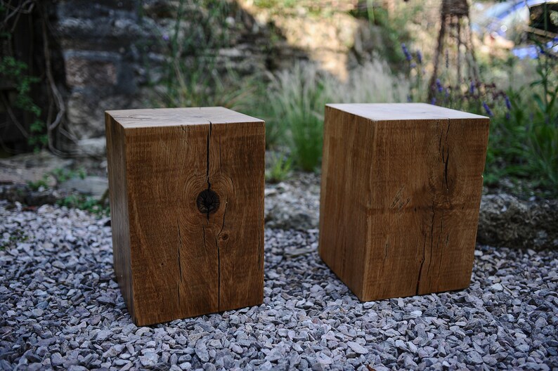 May include: Two rustic wooden stools made from reclaimed wood with a natural brown finish. The stools are sitting on a bed of small gray gravel.