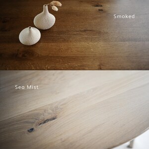 Puede incluir: Una imagen dividida que muestra dos superficies de madera. La secci&oacute;n superior est&aacute; etiquetada como Smoked y presenta una veta de madera marr&oacute;n oscuro con dos peque&ntilde;os jarrones blancos texturizados. La secci&oacute;n inferior est&aacute; etiquetada como Sea Mist y muestra una veta de madera beige claro.