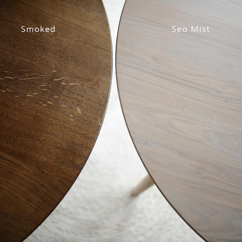Puede incluir: Primer plano de dos tableros de mesa redondos de madera. Uno es marr&oacute;n oscuro, etiquetado como "Smoked", y el otro es gris claro, etiquetado como "Sea Mist". La veta de la madera es visible en ambas superficies, mostrando la textura natural y las variaciones de color.