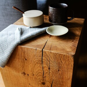 May include: A wooden end table with a blue and white striped towel draped over it. There are three ceramic dishes on the table, including a small white sugar bowl with a spoon, a brown mug, and a small white saucer.