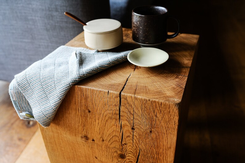 May include: A wooden end table with a blue and white striped towel draped over it. There are three ceramic dishes on the table, including a small white sugar bowl with a spoon, a brown mug, and a small white saucer.