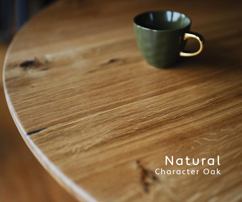 Puede incluir: Una mesa redonda de roble natural con vetas y nudos visibles, con una taza de cer&aacute;mica verde oliva oscuro con asa dorada encima. El texto Natural Character Oak est&aacute; impreso en blanco en la esquina inferior derecha de la imagen.