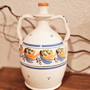 May include: A white ceramic pitcher with two handles and a blue and orange floral design. The pitcher has a small spout and a rounded base.