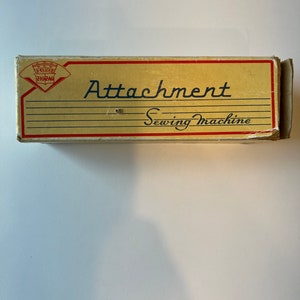 May include: A vintage cardboard box for a sewing machine attachment. The box is beige with red and black lettering. The text on the box reads "Deluxe Zig Zag Attachment Sewing Machine".
