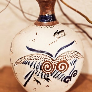 May include: A white ceramic vase with a brown and blue bird design. The vase has a round body and a narrow neck.