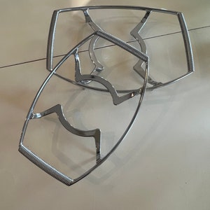 May include: Two chrome wire cooling racks, one stacked on top of the other. The racks are designed to hold hot dishes or baked goods.