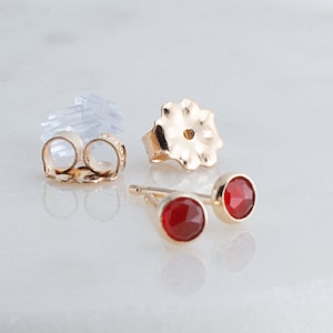 May include: A pair of gold stud earrings with red gemstone accents. The earrings have a simple, classic design and are perfect for everyday wear.