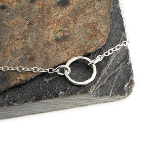 May include: A delicate silver necklace featuring a thin, polished chain and a single, small circular pendant. The necklace is constructed from fine metallic links that form a continuous loop, showcasing a simple and clean design with a bright finish.