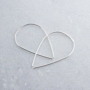 May include: A pair of silver teardrop shaped hoop earrings. The earrings are made of thin wire and have a simple, minimalist design.