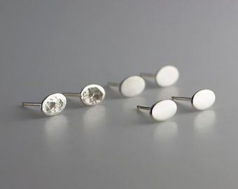 May include: Four pairs of silver oval stud earrings. Two pairs are smooth and two pairs have a hammered texture.