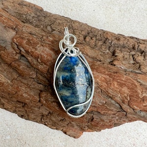 May include: A silver wire wrapped pendant featuring a blue and grey oval lapis lazuli gemstone.