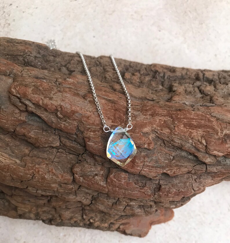 May include: A silver chain necklace with a teardrop-shaped iridescent crystal pendant.