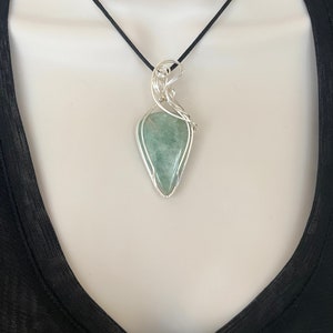 May include: A silver wire wrapped pendant featuring a green gemstone. The pendant is hanging from a black cord.