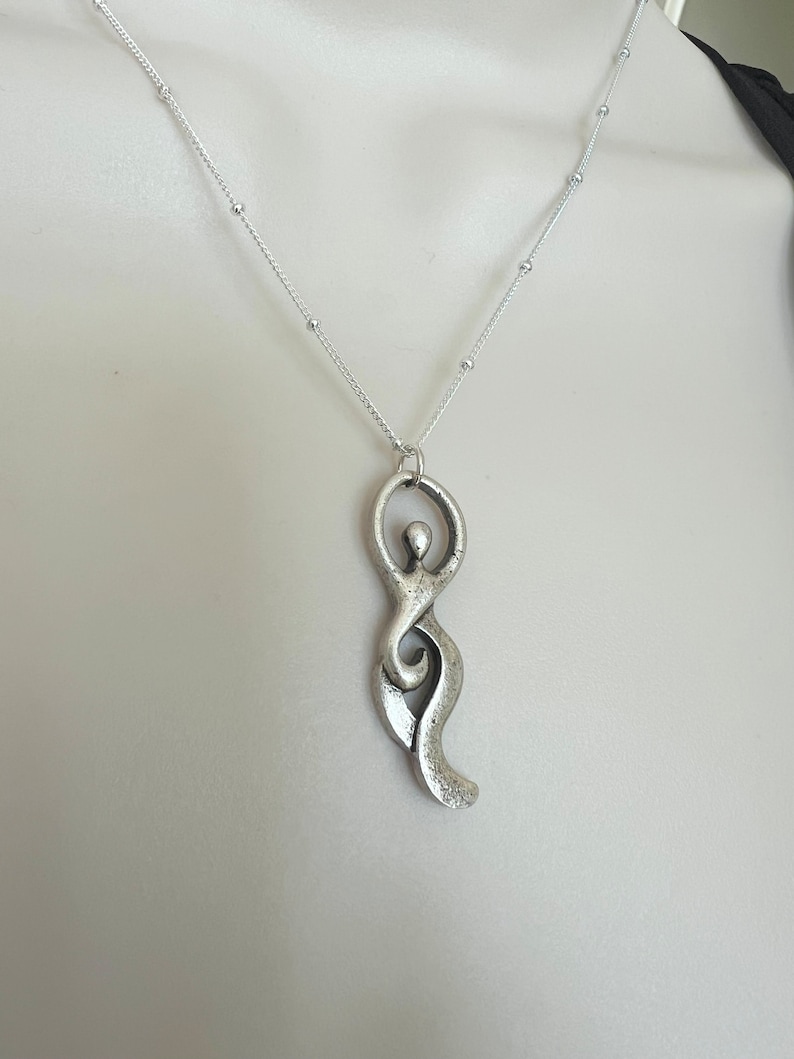 Pu&ograve; includere: Una collana d'argento con un ciondolo a forma di figura umana stilizzata. Il ciondolo &egrave; in metallo e ha una superficie testurizzata.