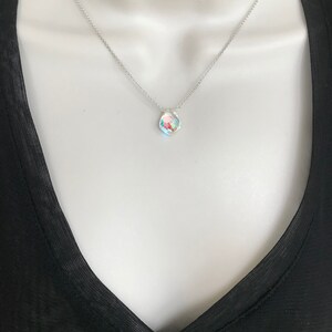 May include: A silver chain necklace with a small, iridescent, faceted gemstone pendant.