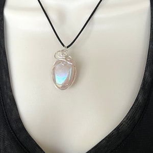 May include: A silver wire wrapped pendant featuring a iridescent, light pink, oval shaped gemstone. The pendant is hanging from a black cord.